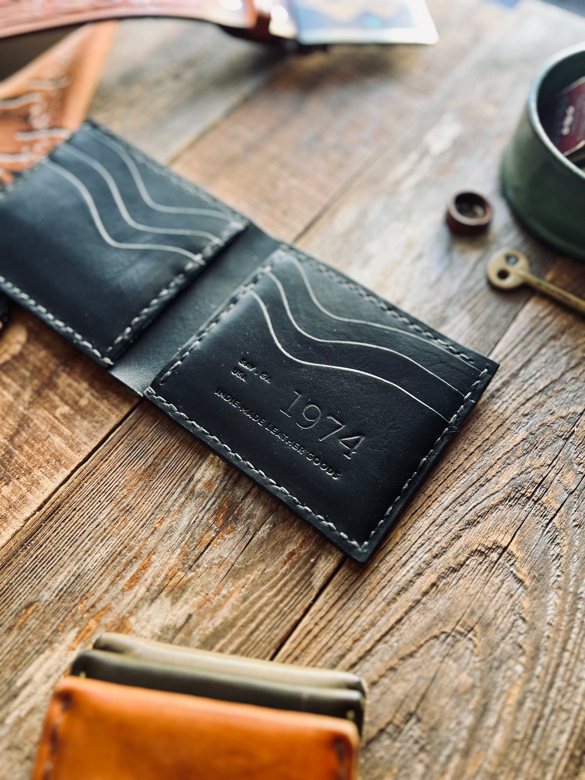 Black leather wallet with '1974' engraving on a wooden surface