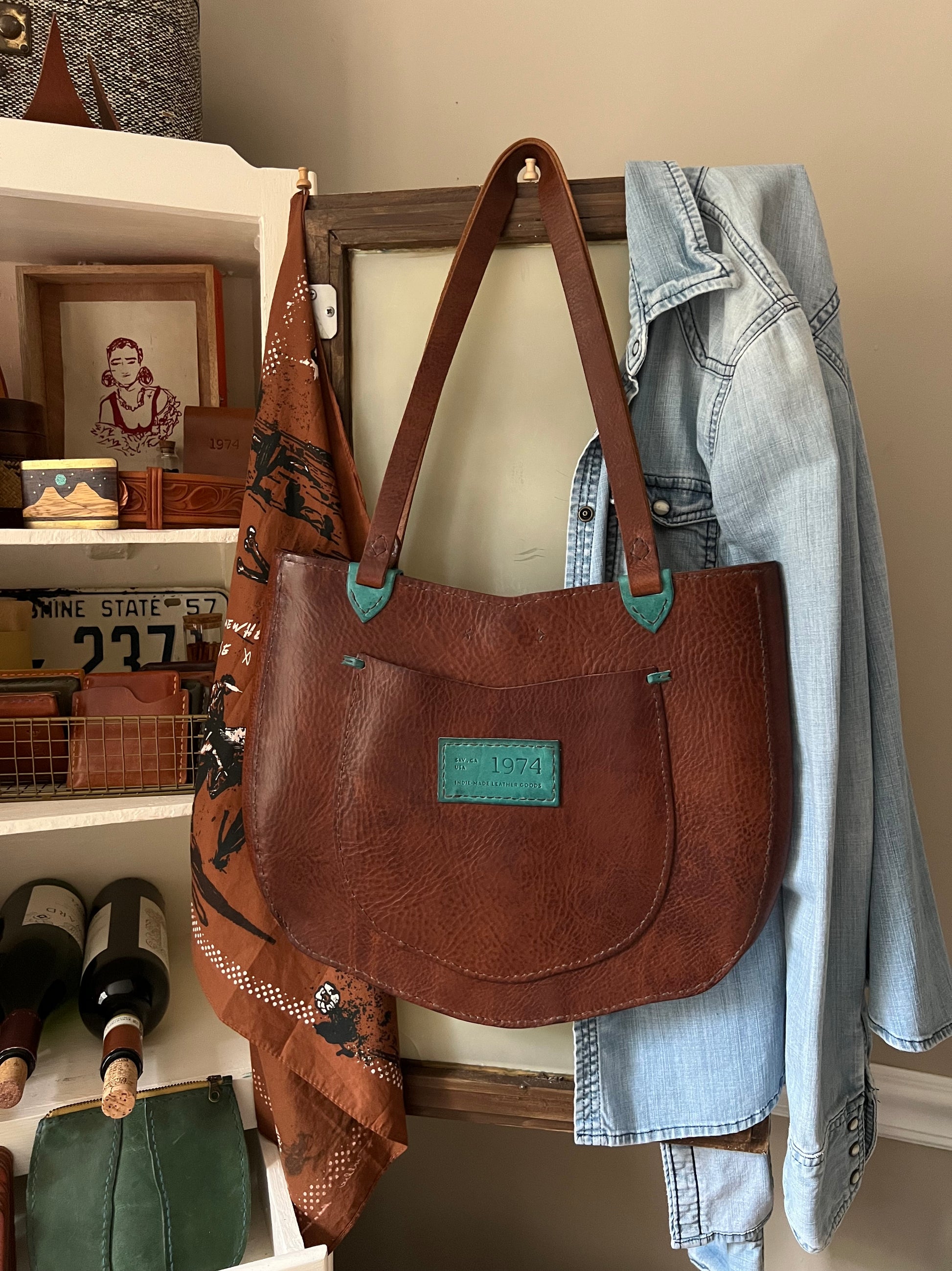 Brown leather handbag with green accents on a shelf with clothes and bottles