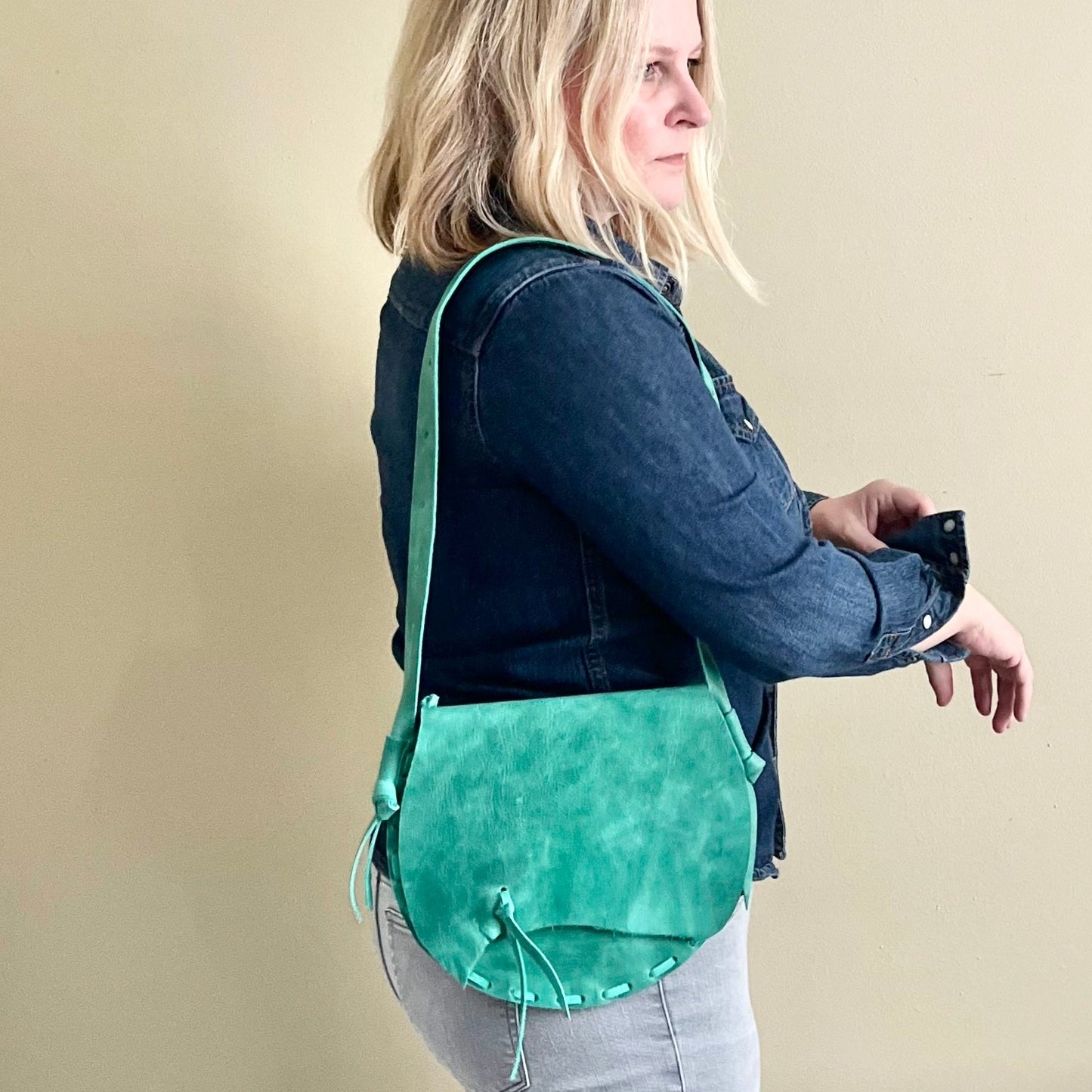 Woman wearing a green crossbody bag against a beige background