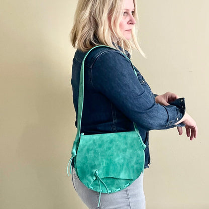 Woman wearing a green crossbody bag against a beige background