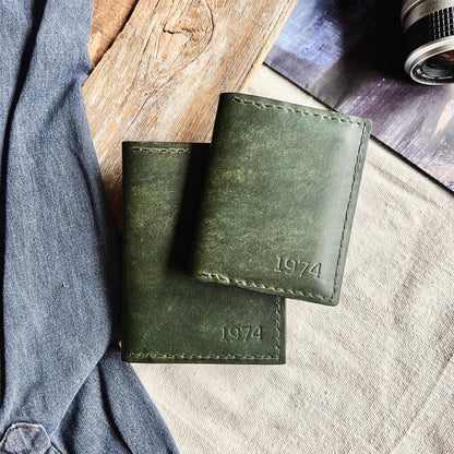 Two artisan made leather wallets on a layered and textured background of woods and canvas with denim and an old camera within view.