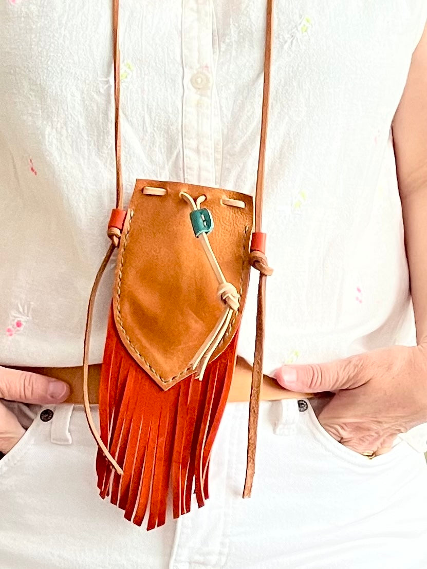 Tan and tangerine leather artisan micro pouch with fringes held by a person wearing a white shirt.